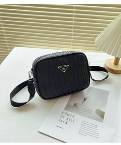 Detail of black woven camera bag featuring golden triangular metal logo and wide strap