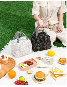 Detail of tweed insulated lunch bags in black and white with striped handles on grass