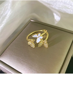 Close-up of golden butterfly ring with white enamel and zircon stones on a jewelry box