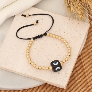 Detail of beaded evil eye bracelet with golden beads on black adjustable woven cord