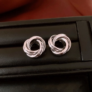 Détail macro de boucles d'oreilles nœud triple entrelacées en argent dans un écrin noir