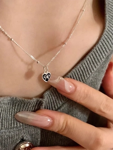 Close-up of S925 silver heart necklace with black enamel and white bow pendant detail