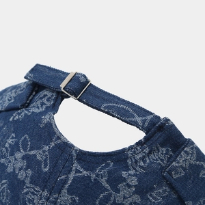 Detail of adjustable metal buckle and floral denim texture on a navy blue docker hat