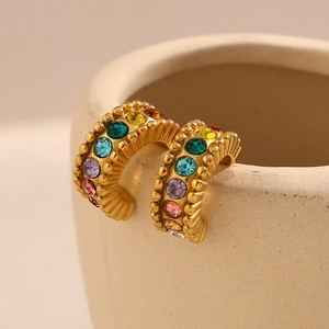 Close-up of gold C-shaped earrings with colorful zircon stones on ceramic edge