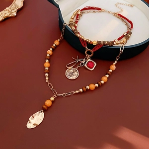 Detail of layered necklace with gold leaf, red gemstone, and butterfly coin pendants