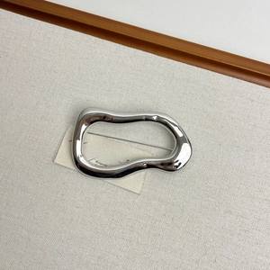 Detail view of irregular liquid-metal silver brooch on beige textured fabric surface