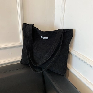 Close-up of black corduroy tote bag showing soft ribbed texture and fashion woven label