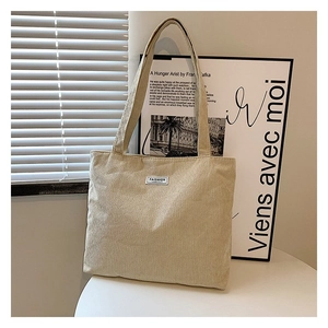 Detailed close-up of cream corduroy tote bag featuring small Fashion woven label on surface