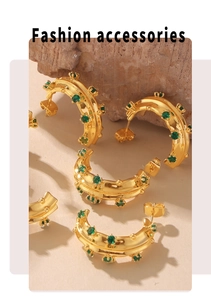Detailed close-up of C-shaped 18k gold earrings with emerald green glass stones on a rock