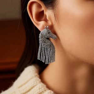 Close-up of sparkling horse head drop earrings with silver tassels on a female model