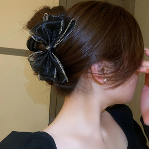 Détail de la pince à cheveux avec nœud en tulle noir, bordure dorée et cristal central