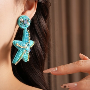 Detailed shot of large turquoise starfish earring with beads and rhinestones on model