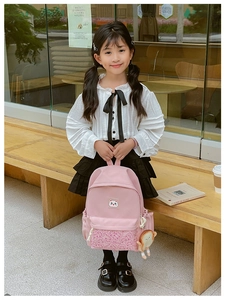 Pink school backpack with cat patch and plush toast pendant shown in a bright outdoor setting