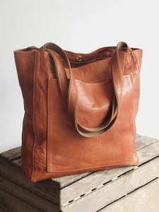 Gros plan d'un cabas vintage en cuir marron avec poche avant sur une caisse en bois