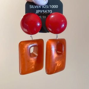 Macro shot of red glossy orb and orange acrylic pendant on S925 silver needle earrings