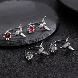 Detailed view of hummingbird and flower open rings with colorful gemstones on black stone