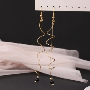 Detail of gold spiral tassel earrings with black beads on a soft pink fabric display