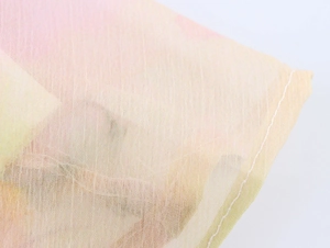 Dettaglio in primo piano del tessuto chiffon con sfumature gialle e rosa e orlo cucito