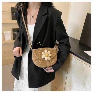 Detail of woven khaki saddle bag featuring a white daisy plush and long shoulder strap