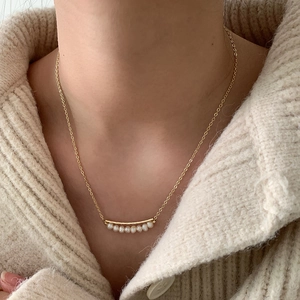 Elegant gold-plated baroque freshwater pearl necklace with curved pendant on beige knit