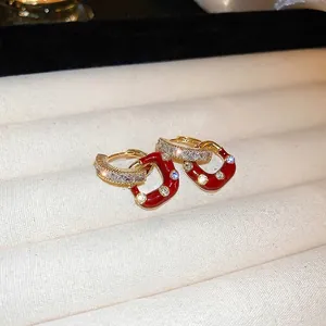 Elegant gold C-shaped earrings with red enamel and zircon stones on a white tray
