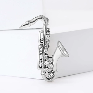 Silver saxophone brooch with sparkling rhinestones on a white minimalist background