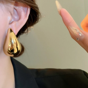 Close-up of a model wearing large polished gold teardrop earrings with a glossy finish