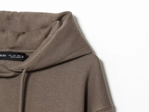 Detailed view of brown knit hoodie neckline showing drawstring and inner size label
