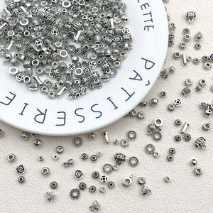 Assorted silver vintage engraved metal beads in a white ceramic dish for DIY jewelry