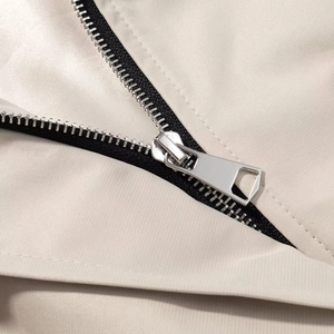 Detail of silver metal zipper with black tape on beige belted trench coat fabric