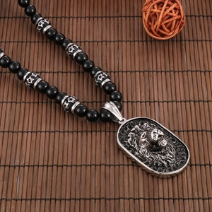 Close-up of a silver lion head pendant with black beaded necklace on a bamboo mat
