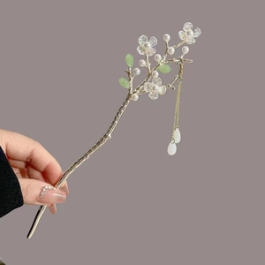 Detail of a metal hair stick with magnolia flowers, green leaves and hanging tassels