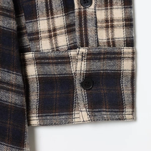 Dettaglio del polsino di una camicia a quadri blu e beige con bottone e trama in flanella