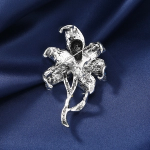 Vintage silver lily flower brooch with textured metal finish on deep blue silk backdrop