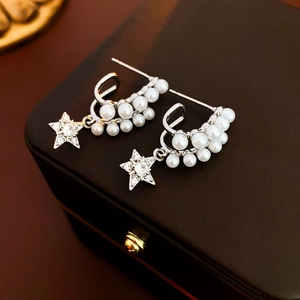 Macro shot of C-shaped pearl earrings with sparkling star charms on a jewelry box