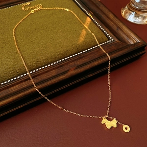 Detail of gold plated necklace with dog pendant and coin charm on a green fabric