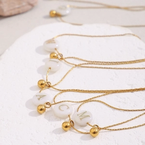 Detail of 18K gold plated necklaces with white shell alphabet pendants on white stone