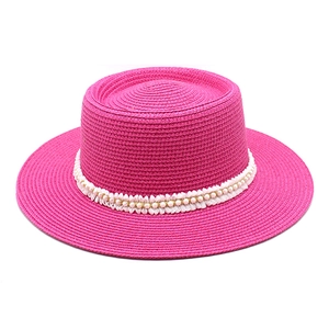 Detail of bright pink boater hat featuring woven straw texture and pearl bead trim band