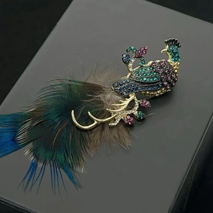 Elegant peacock brooch with colorful crystals and real feathers on a premium display box