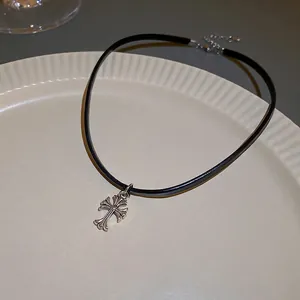 Faux leather choker with vintage silver cross pendant on a white textured ceramic plate