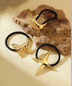 Detailed view of three gold metal hair ties with butterfly and star charms on rock sand