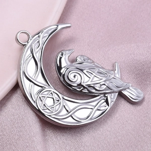 Detailed macro view of silver stainless steel crescent moon and crow pendant on pink silk