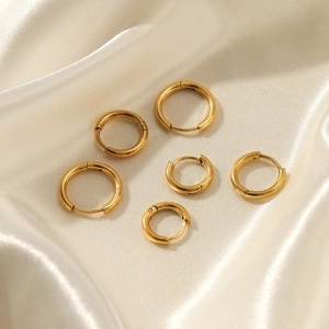 Three pairs of polished gold stainless steel hoop earrings in varied sizes on silk
