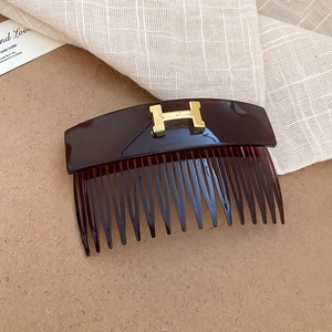 Close-up of a tortoiseshell acrylic hair comb featuring a gold H-shaped metal logo