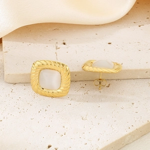 Macro shot of square gold earrings with white gemstone and textured edges on silk cloth
