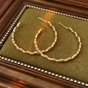 Detail of gold-plated wavy C-shape earrings in a vintage velvet jewelry box