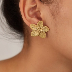 Detailed close-up of golden five-petal flower stud earring with brushed metal texture