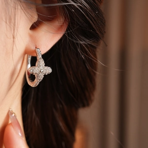 Close-up of elegant silver clover hoop earrings with pavé zircons on a female model