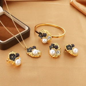 Detailed set of gold jewelry with white pearls and black flowers on silk background