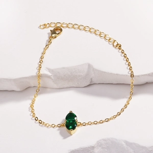 Detailed shot of golden heart bracelet with emerald green stone and lobster clasp